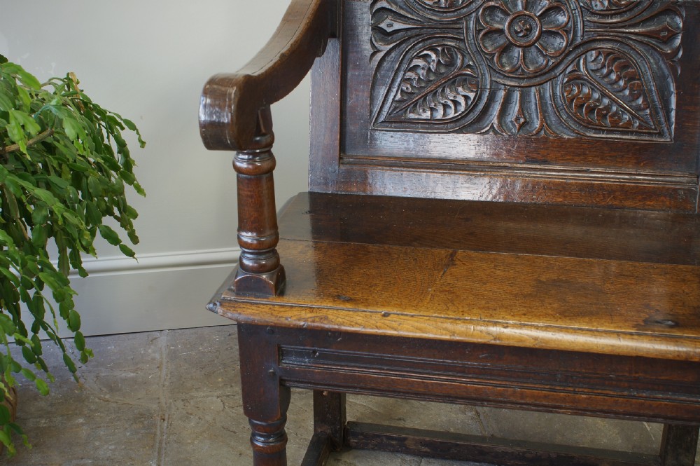 A 17th-century dark oak wainscot armchair with a deeply carved back panel, turned front legs, and sturdy box stretchers. View VII