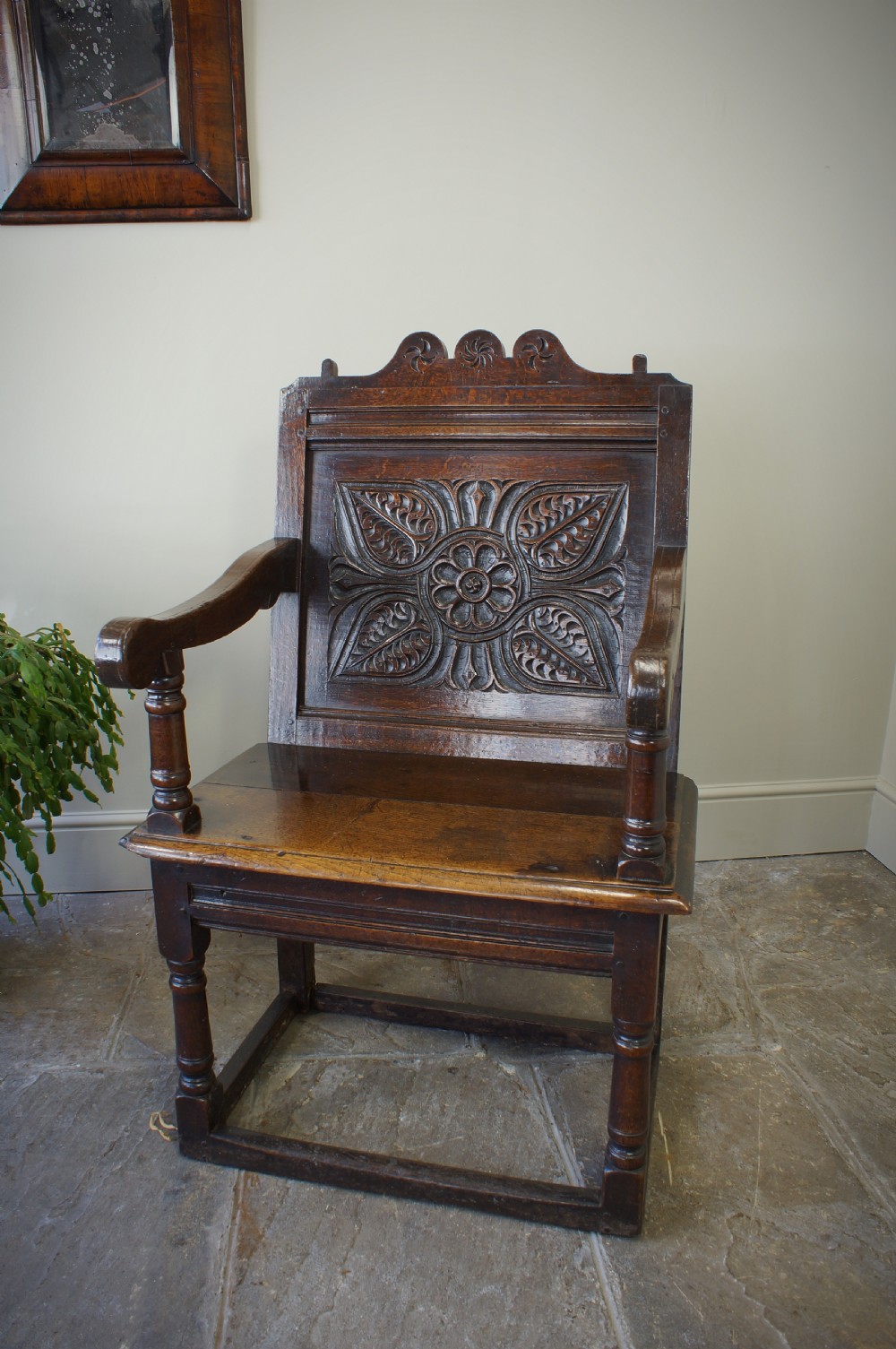 A 17th-century dark oak wainscot armchair with a deeply carved back panel, turned front legs, and sturdy box stretchers. View VIII