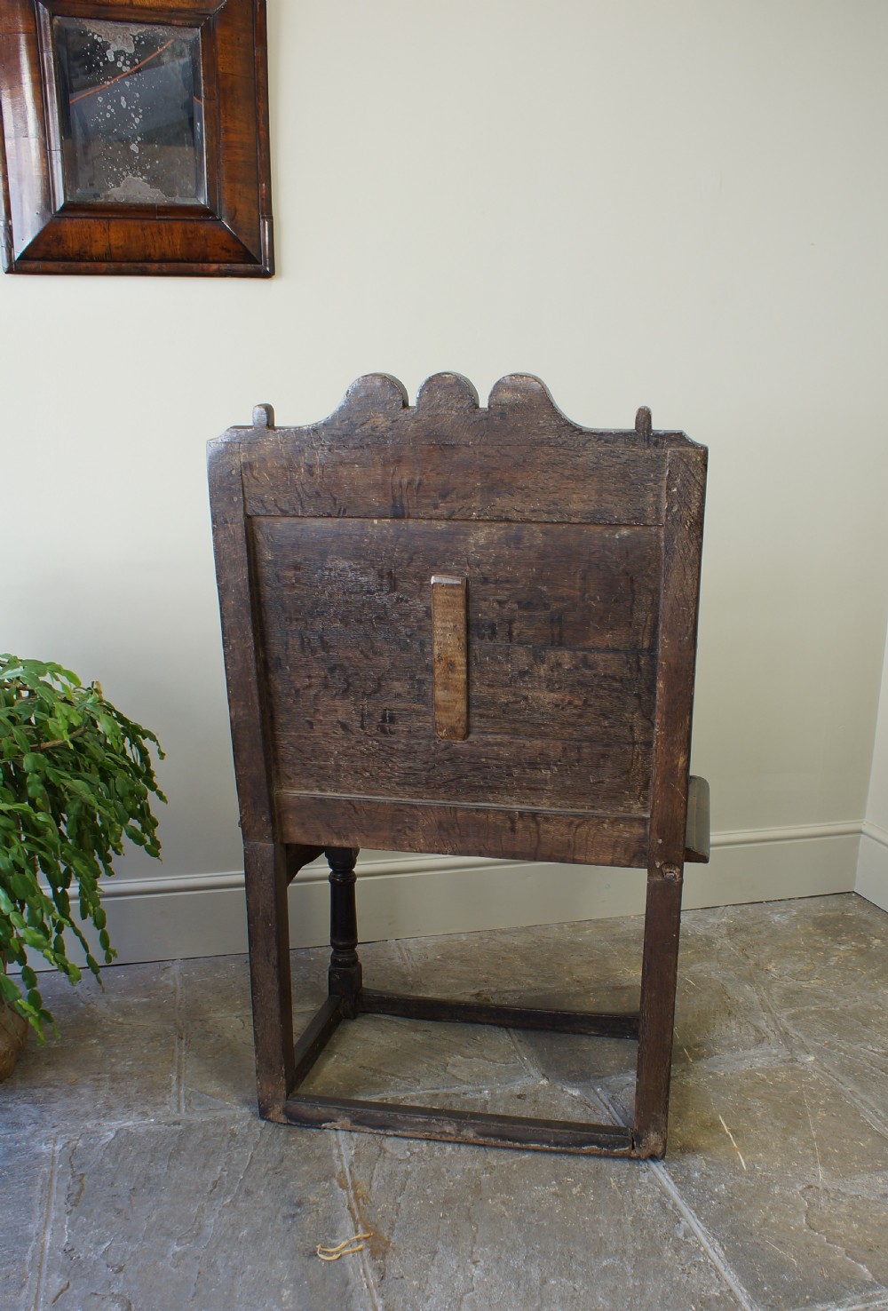 A 17th-century dark oak wainscot armchair with a deeply carved back panel, turned front legs, and sturdy box stretchers. View IX