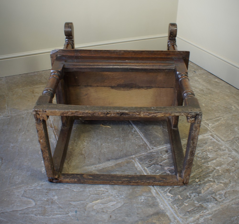 A 17th-century dark oak wainscot armchair with a deeply carved back panel, turned front legs, and sturdy box stretchers. View X