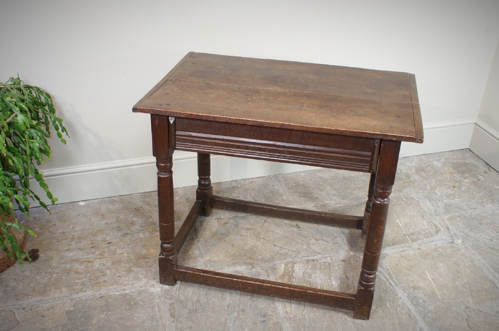 A seventeenth-century dark oak side table featuring a rectangular plank top, moulded apron, turned legs, and perimeter stretchers. View X