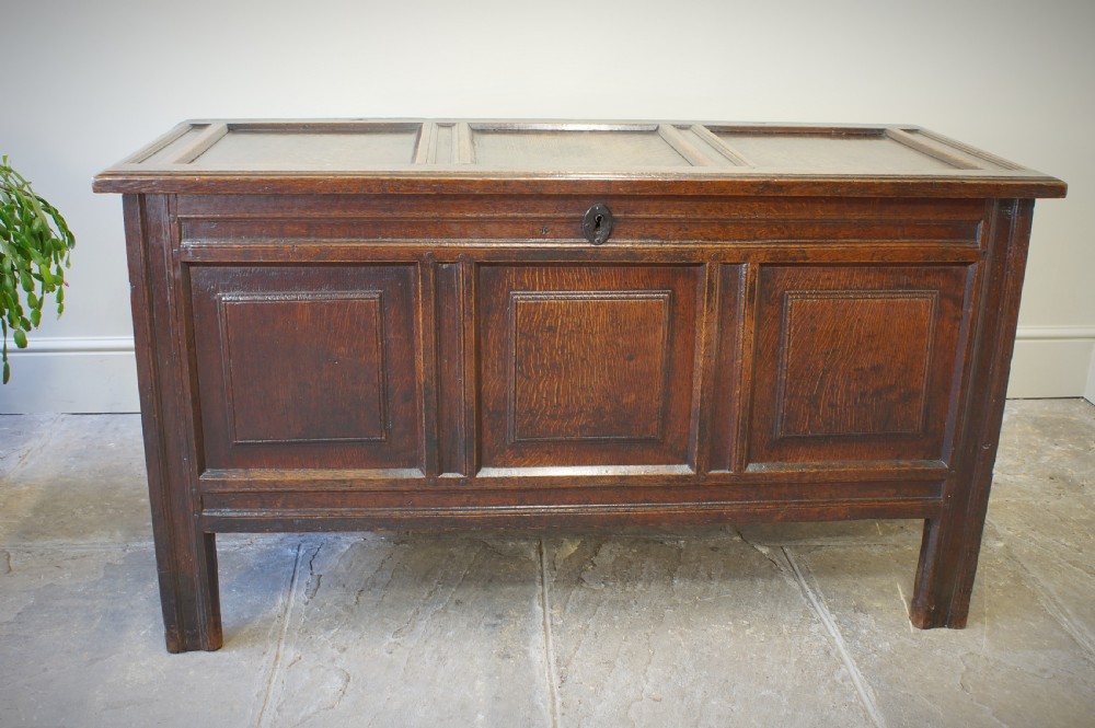 A 17th-century dark oak coffer featuring a three-panel front, hinged lid, and iron keyhole escutcheon resting on stile legs.