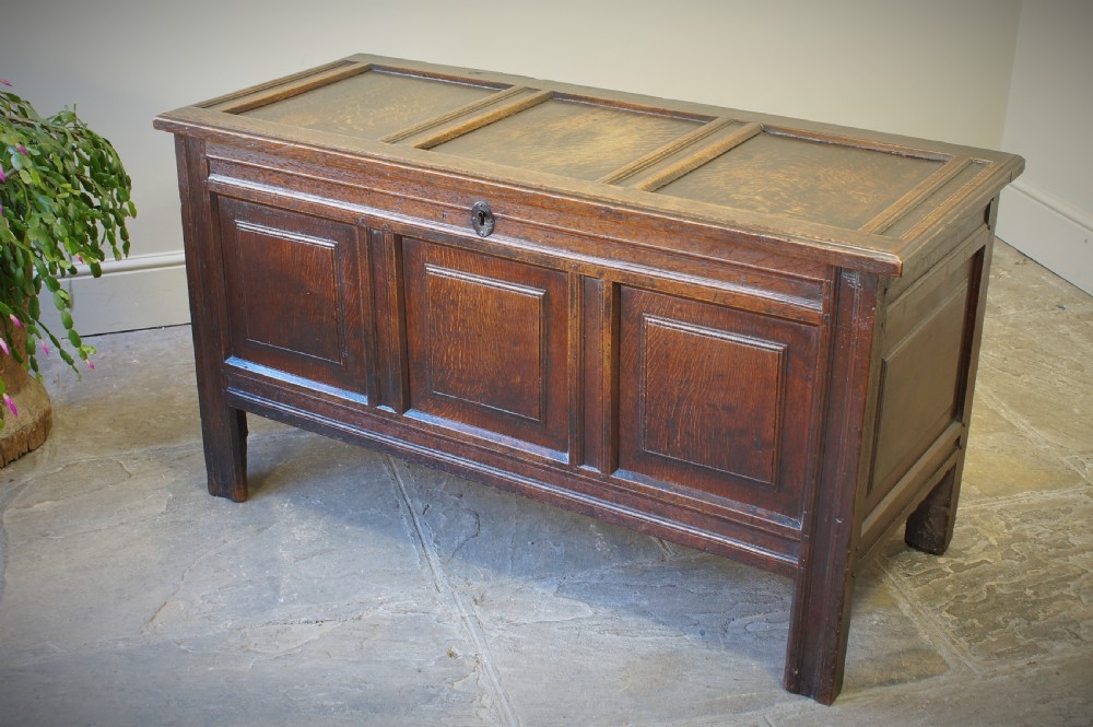 A 17th-century dark oak coffer featuring a three-panel front, hinged lid, and iron keyhole escutcheon resting on stile legs. View II