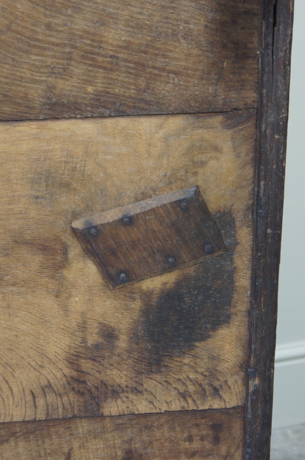 A 17th-century dark oak coffer featuring a three-panel front, hinged lid, and iron keyhole escutcheon resting on stile legs. View V