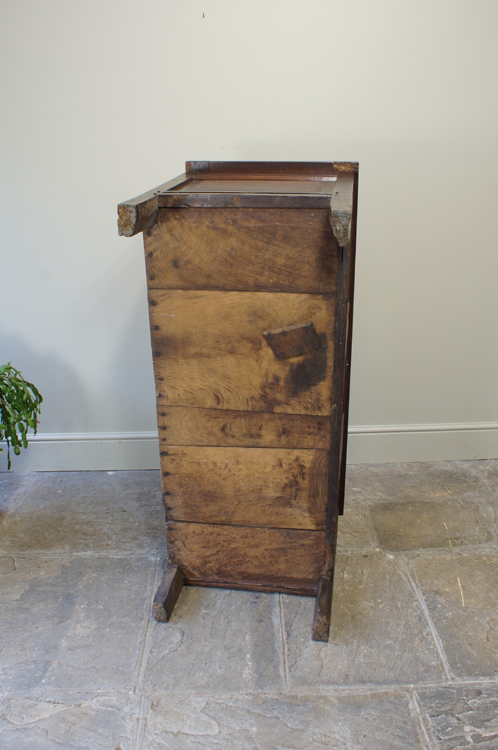 A 17th-century dark oak coffer featuring a three-panel front, hinged lid, and iron keyhole escutcheon resting on stile legs. View VI
