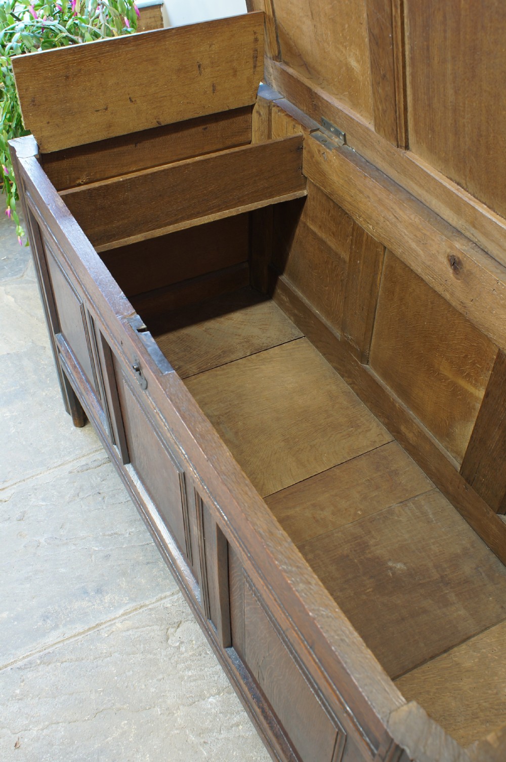 A 17th-century dark oak coffer featuring a three-panel front, hinged lid, and iron keyhole escutcheon resting on stile legs. View VII