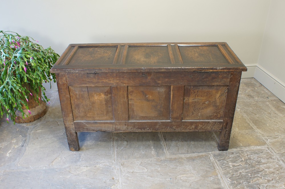A 17th-century dark oak coffer featuring a three-panel front, hinged lid, and iron keyhole escutcheon resting on stile legs. View IX