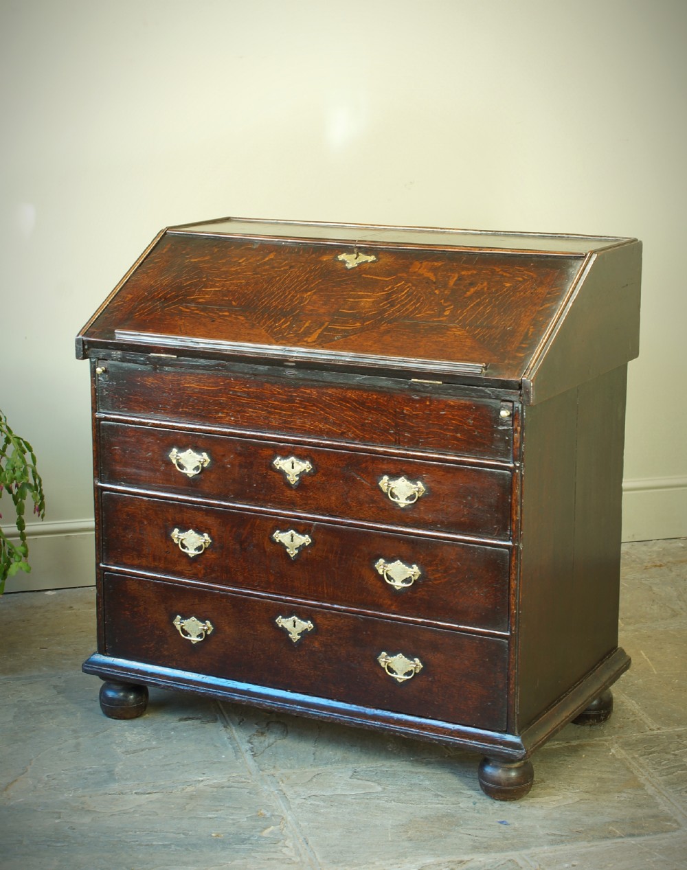 A William and Mary dark oak slant-front bureau featuring geometric parquetry on the lid, three long drawers with brass drop handles, and bun feet. View VI