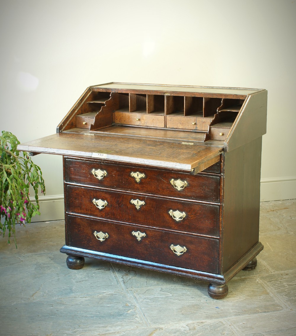 A William and Mary dark oak slant-front bureau featuring geometric parquetry on the lid, three long drawers with brass drop handles, and bun feet. View V