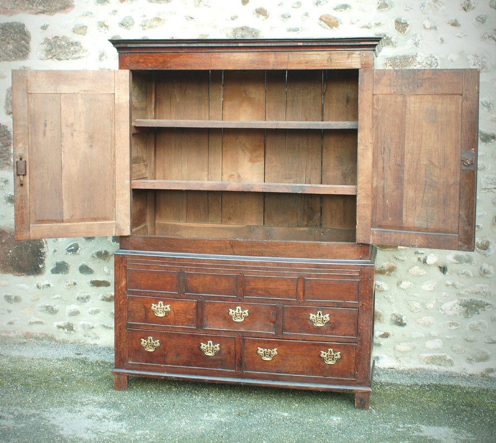 A Georgian oak linen press featuring two arched upper panel doors over a lower chest section with decorative brass hardware. View III