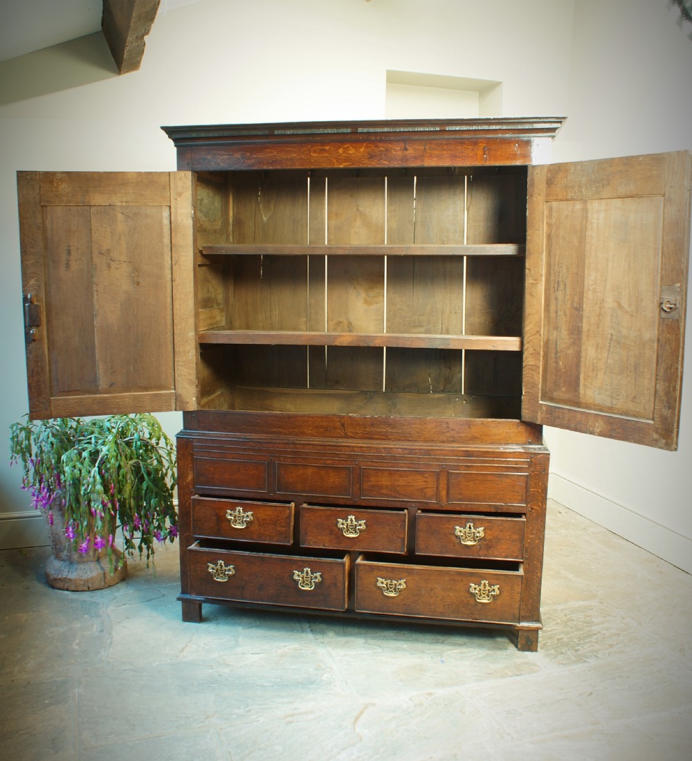 A Georgian oak linen press featuring two arched upper panel doors over a lower chest section with decorative brass hardware. View VIII