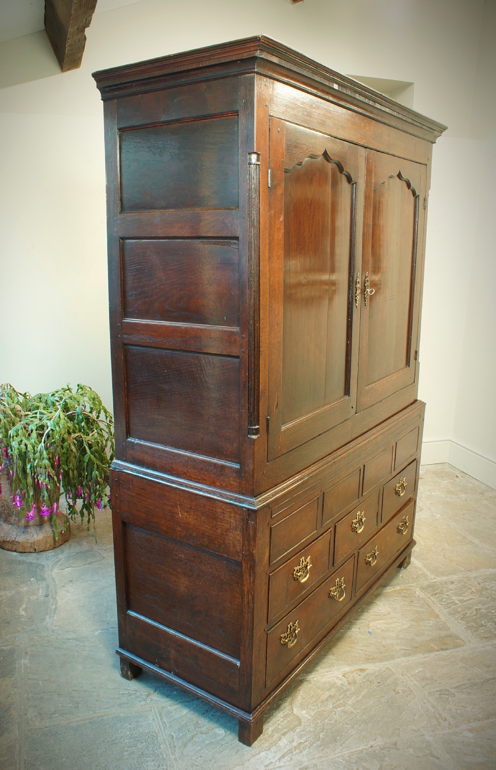 A Georgian oak linen press featuring two arched upper panel doors over a lower chest section with decorative brass hardware. View IX