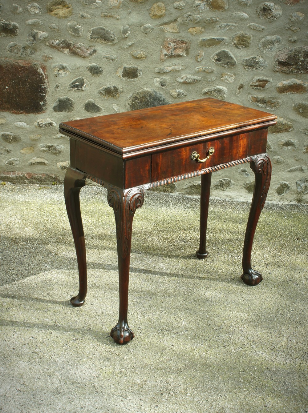 A George II mahogany fold-over card table featuring carved cabriole legs with ball-and-claw feet and a central drawer.