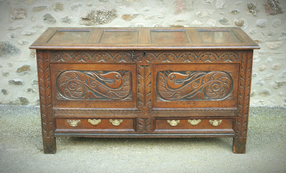 A 17th century dark oak mule chest featuring carved scrollwork front panels, two lower drawers with brass handles, and a panelled top lid. View III