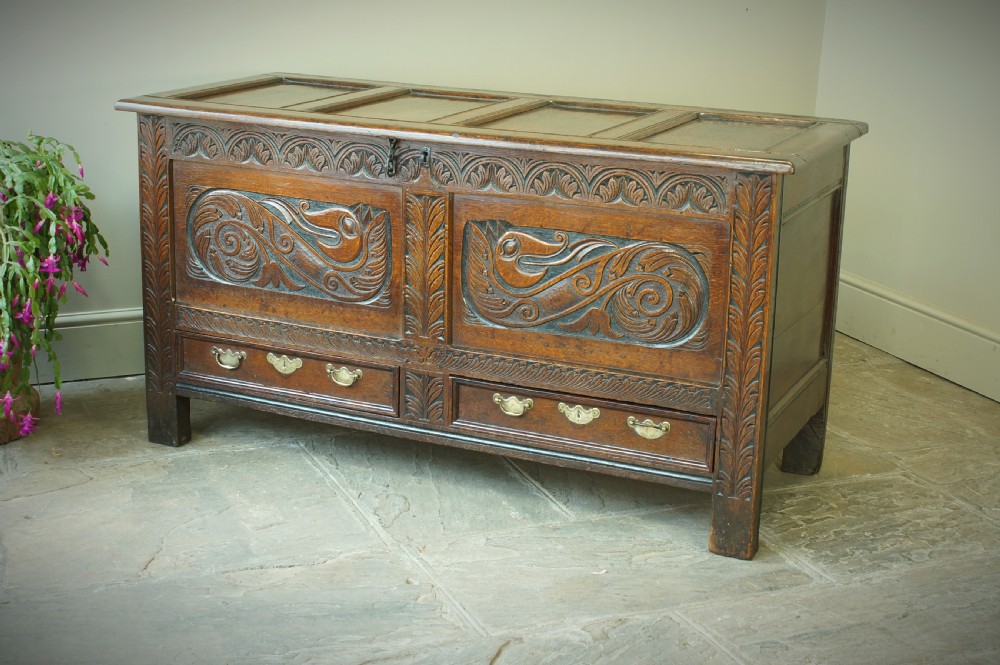 A 17th century dark oak mule chest featuring carved scrollwork front panels, two lower drawers with brass handles, and a panelled top lid. View II