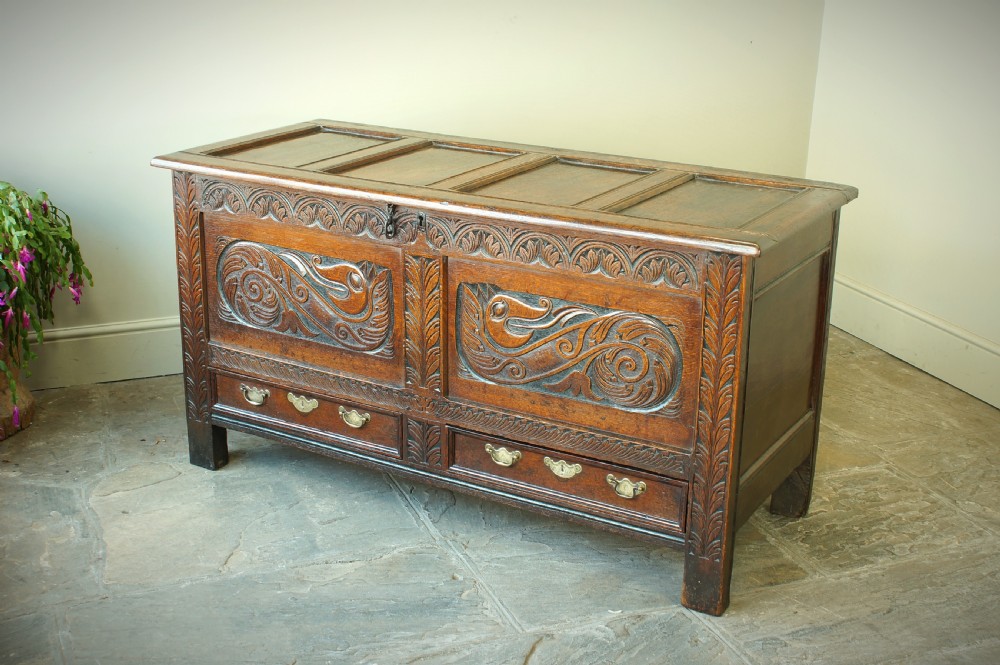A 17th century dark oak mule chest featuring carved scrollwork front panels, two lower drawers with brass handles, and a panelled top lid. View VI