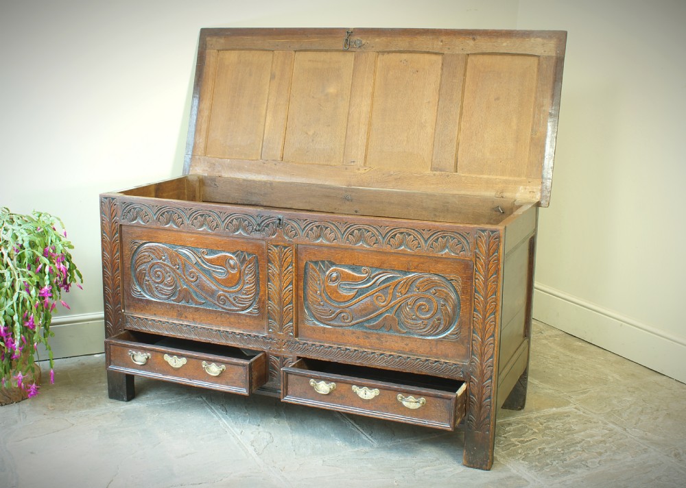 A 17th century dark oak mule chest featuring carved scrollwork front panels, two lower drawers with brass handles, and a panelled top lid. View VIII