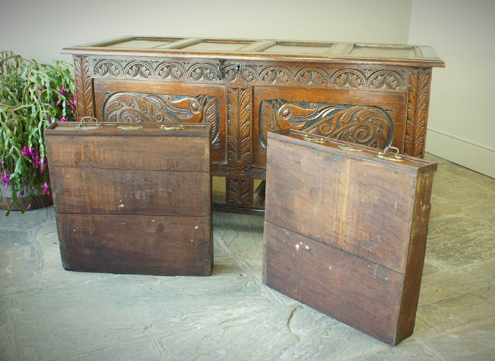 A 17th century dark oak mule chest featuring carved scrollwork front panels, two lower drawers with brass handles, and a panelled top lid. View IX