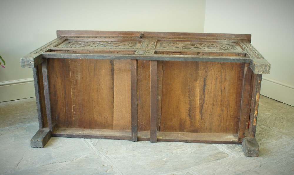 A 17th century dark oak mule chest featuring carved scrollwork front panels, two lower drawers with brass handles, and a panelled top lid. View XIII
