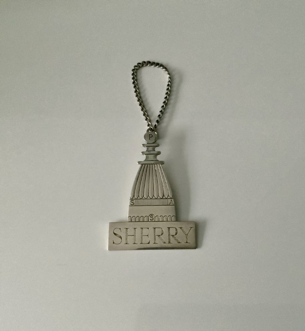 A silver decanter label shaped like an architectural spire above a rectangular plaque engraved with the word SHERRY, attached to a chain.