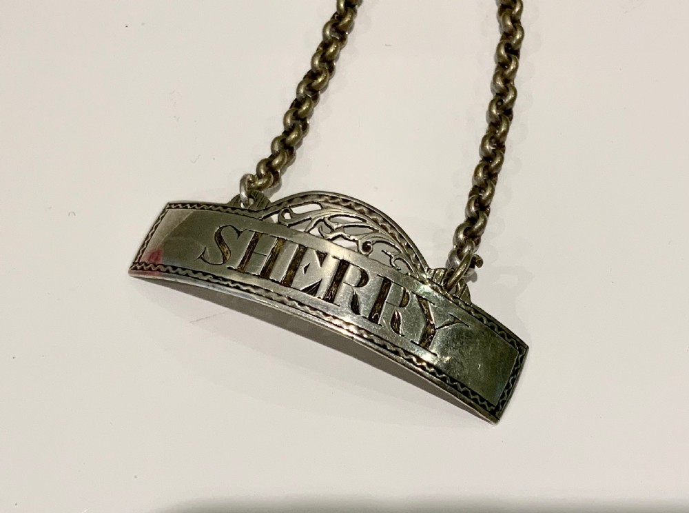 An antique Georgian sterling silver decanter label inscribed with SHERRY, featuring an engraved border, pierced crest, and attached chain. View II