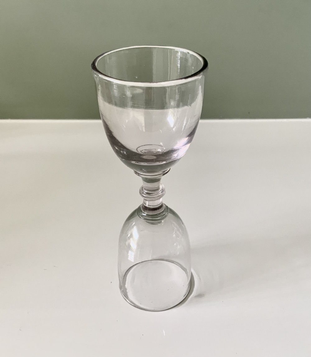 A clear hand-blown Georgian glass dram measure featuring two inverted bell-shaped bowls connected by a central knopped stem. View II