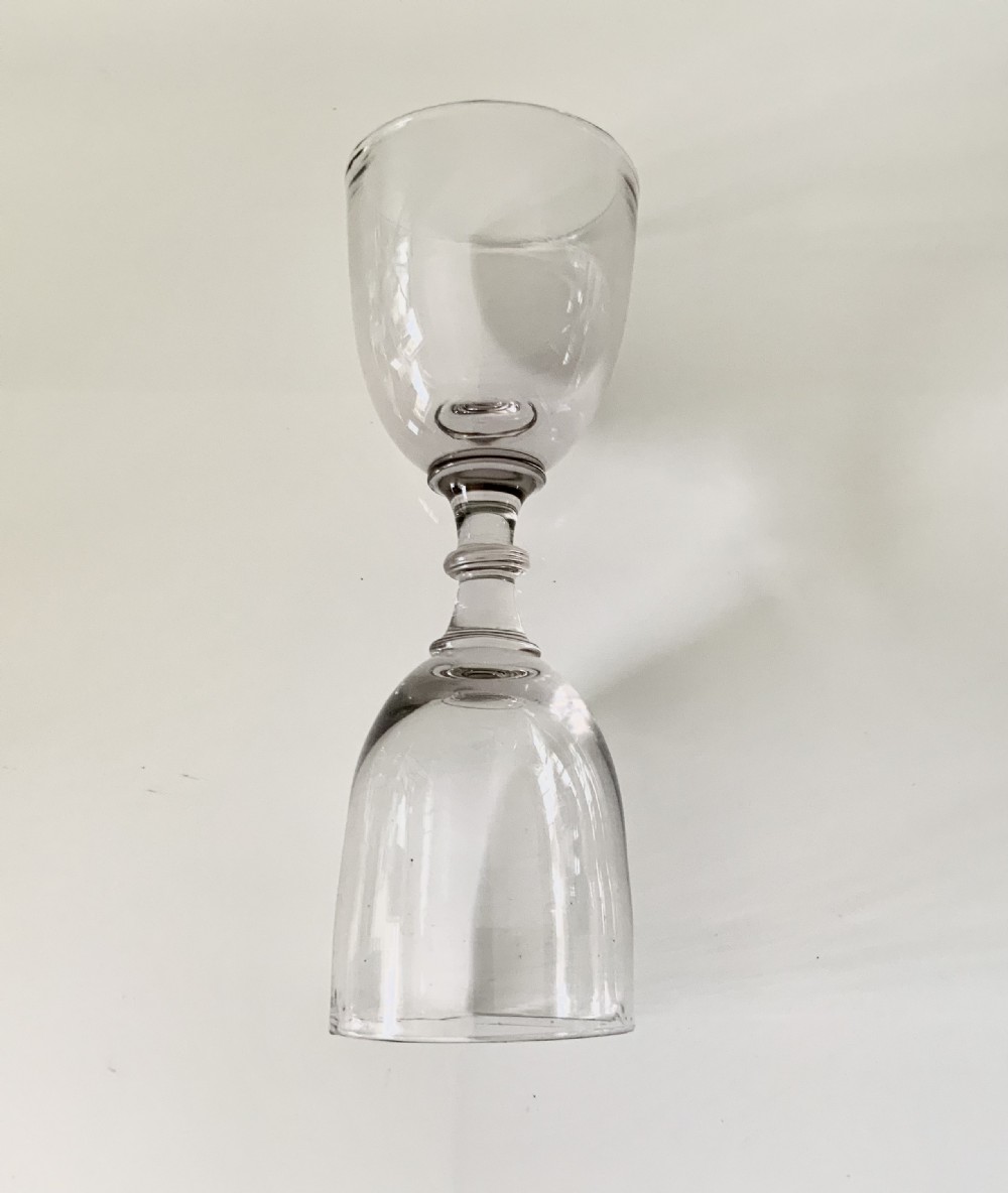 A clear hand-blown Georgian glass dram measure featuring two inverted bell-shaped bowls connected by a central knopped stem. View III
