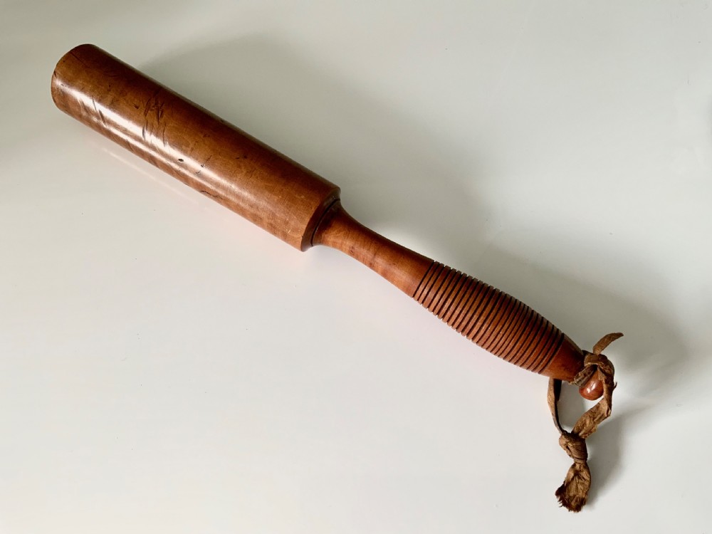 A turned 19th-century satin birch veterinary fleam mallet featuring a cylindrical striking head, a ribbed handle grip, and a tied leather strap.