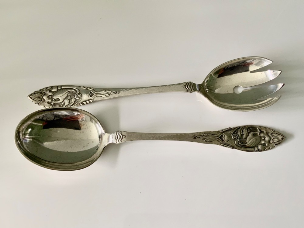 A pair of silver salad servers consisting of a spoon and a three-pronged fork with relief motifs on the handles.