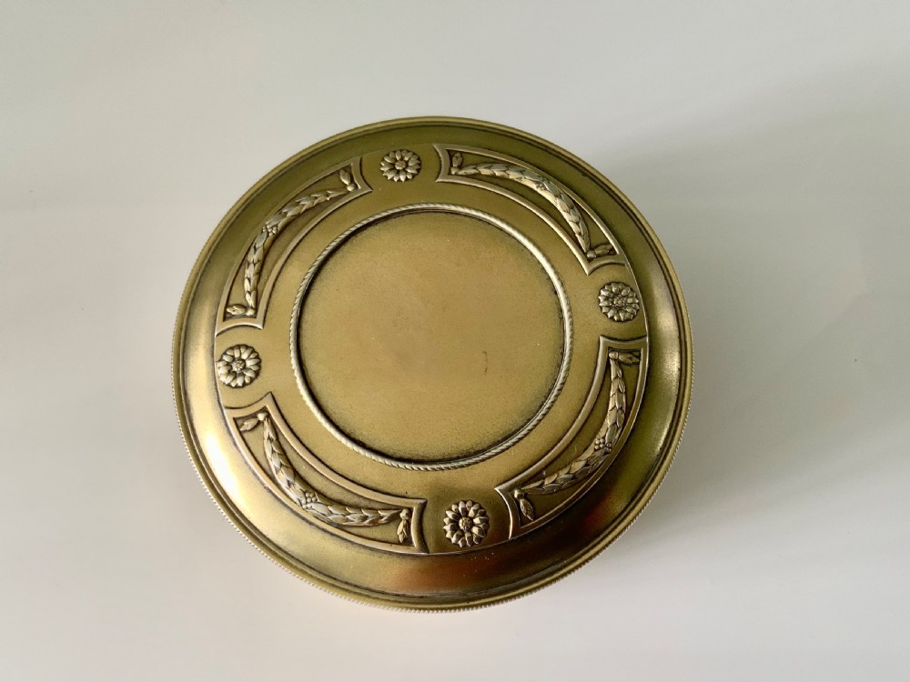Top view of a round French vermeil silver covered bowl featuring relief carvings of floral rosettes and laurel foliage swags.