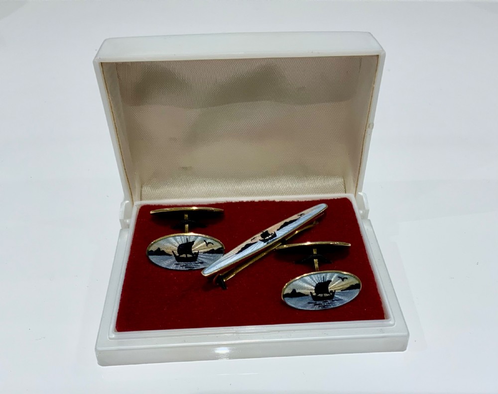 A set of oval silver and enamel cufflinks and a matching tie clip featuring a Viking longship design in blue and white guilloche enamel.