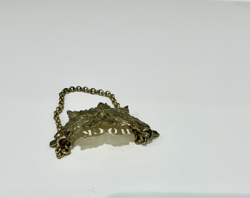 A silver gilt decanter label shaped as a detailed vine leaf with pierced lettering reading HOCK, suspended by a chain. View IV