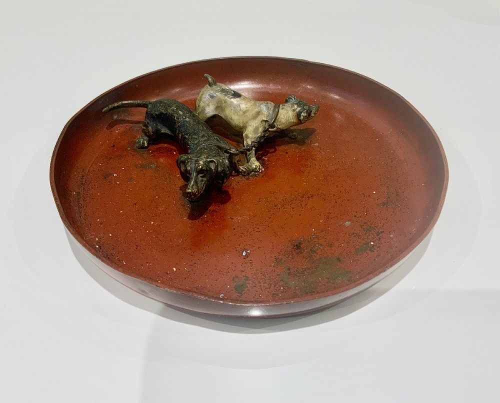 An antique round bronze tray featuring two cold painted dog figures affixed to the interior surface.