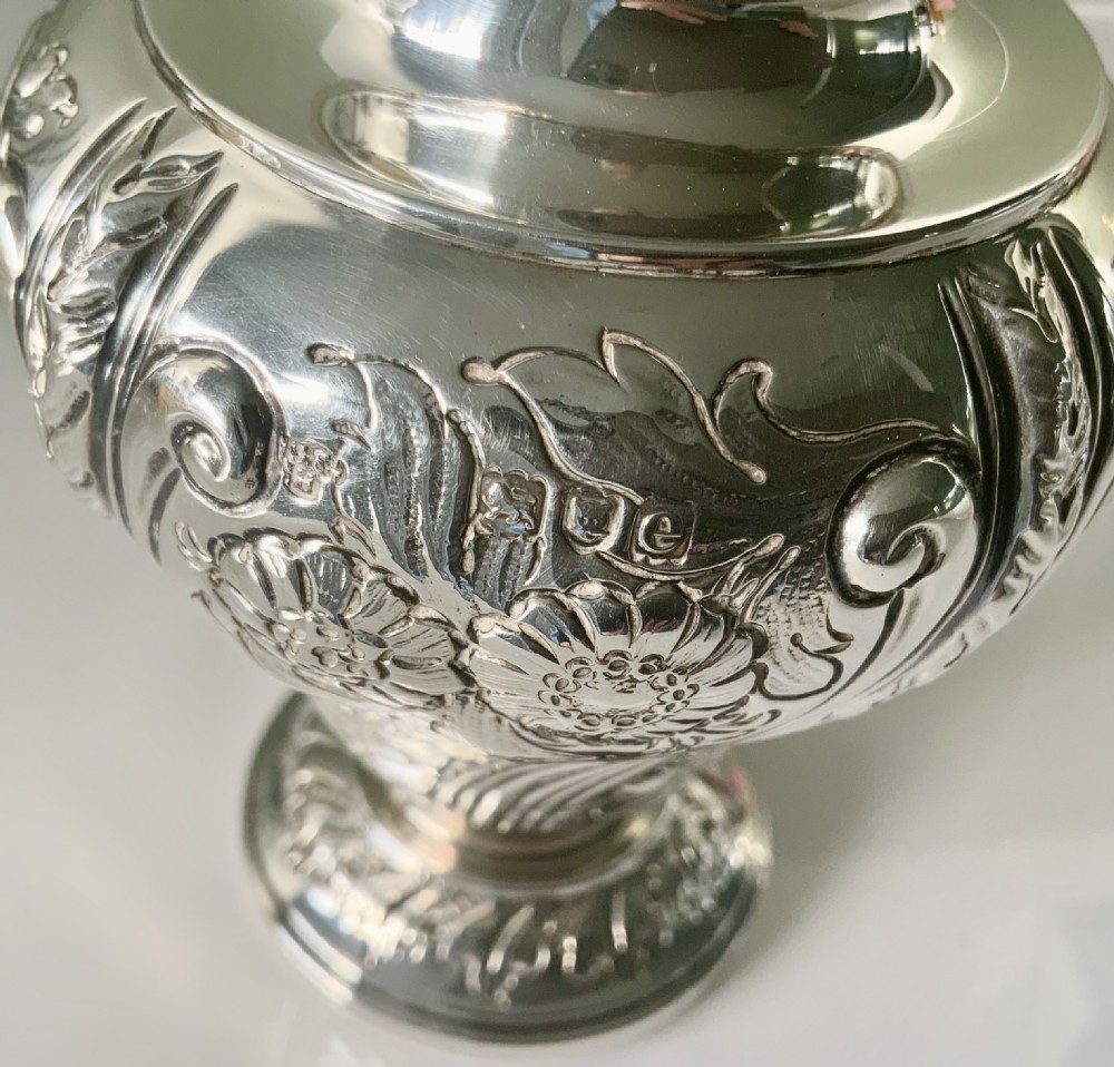 An ornate silver tea caddy featuring embossed scrollwork, a pedestal base, and a decorative finial on the lid. View VII