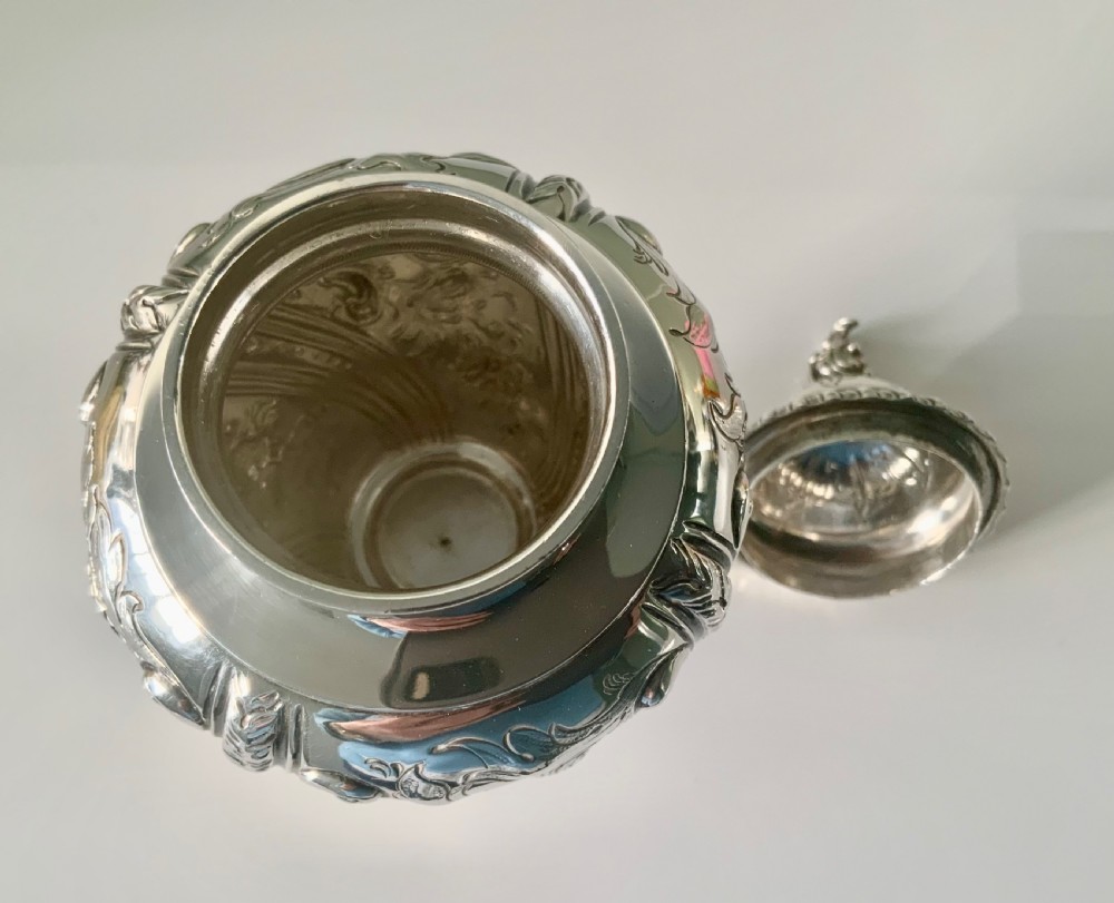 An ornate silver tea caddy featuring embossed scrollwork, a pedestal base, and a decorative finial on the lid. View IX