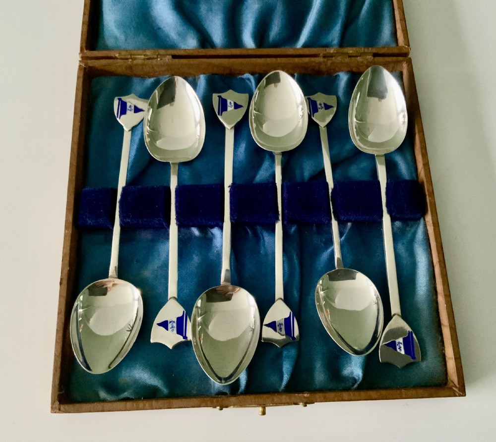 A set of six silver teaspoons with blue and white enamel sailing club flags on shield finials, housed in a blue satin-lined presentation case.