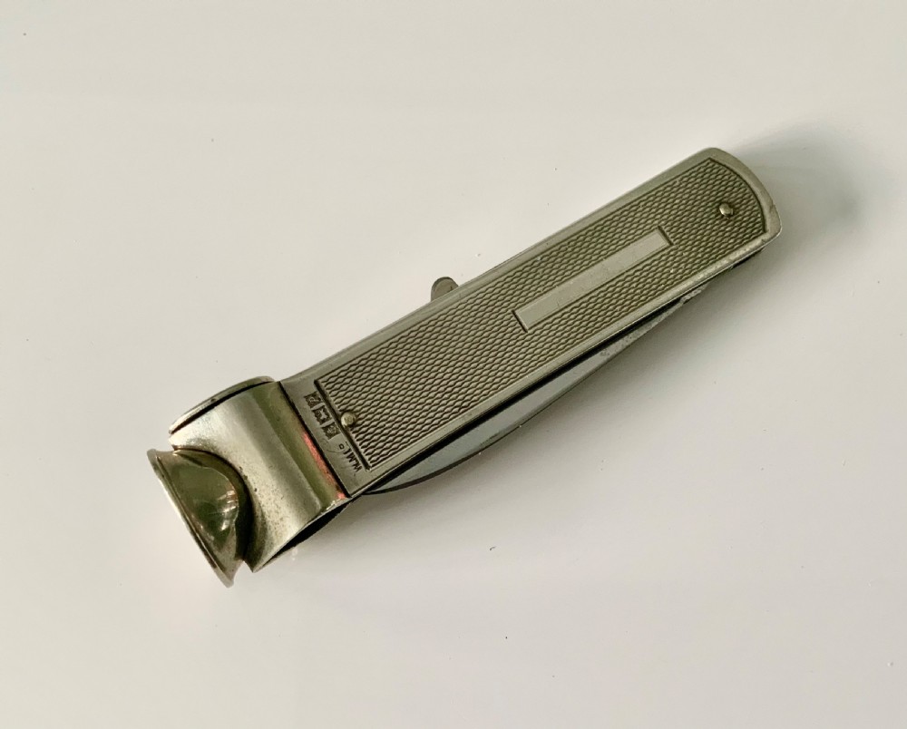 A hallmarked sterling silver pocket knife featuring an engine-turned textured body, a single steel blade, and an integrated cigar cutter at the end. View IV