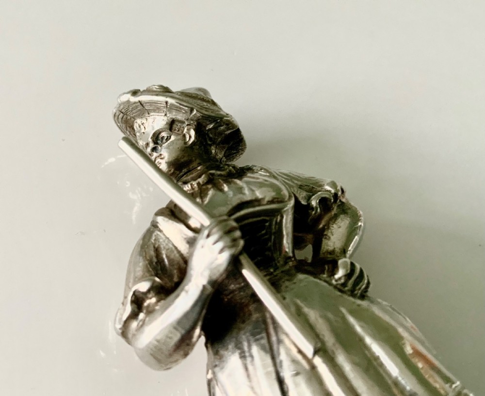 A cast silver perfume bottle sculpted in the form of a standing woman wearing a bonnet and dress while holding a staff. View VI
