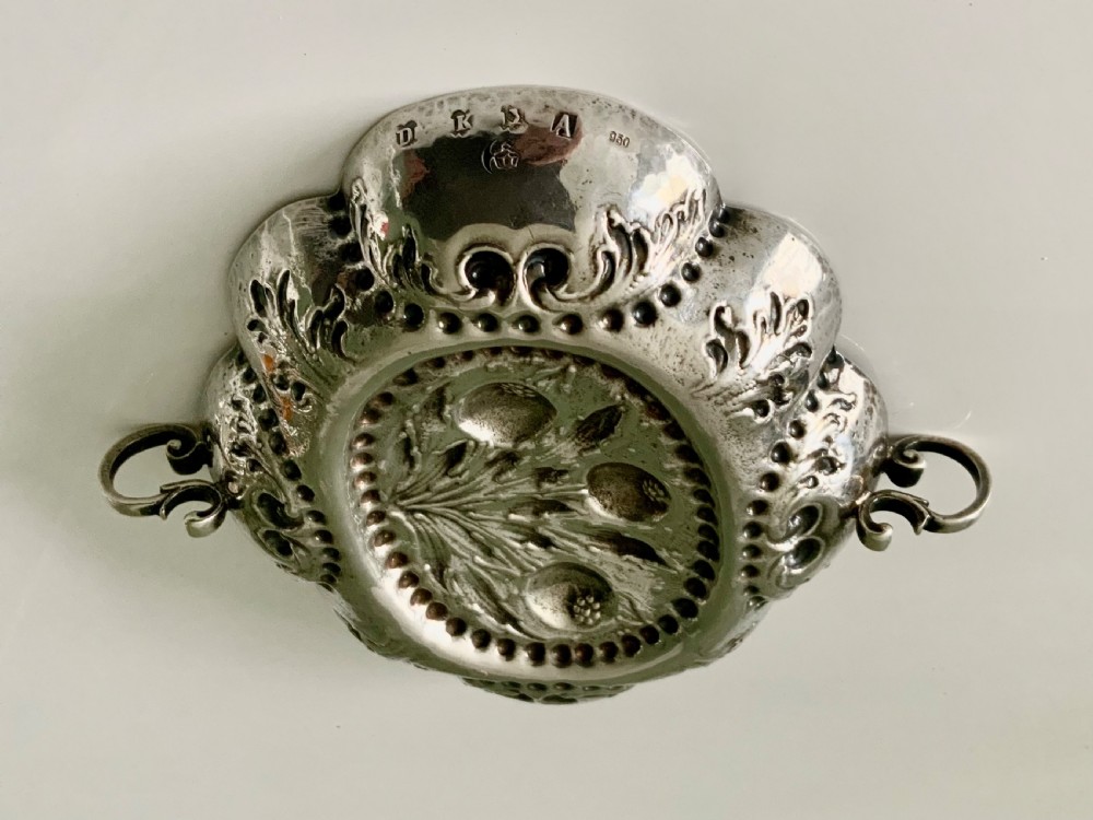 An oval German silver wine taster featuring repousse fruit central decoration, scalloped borders with acanthus scroll details, and loop handles. View II