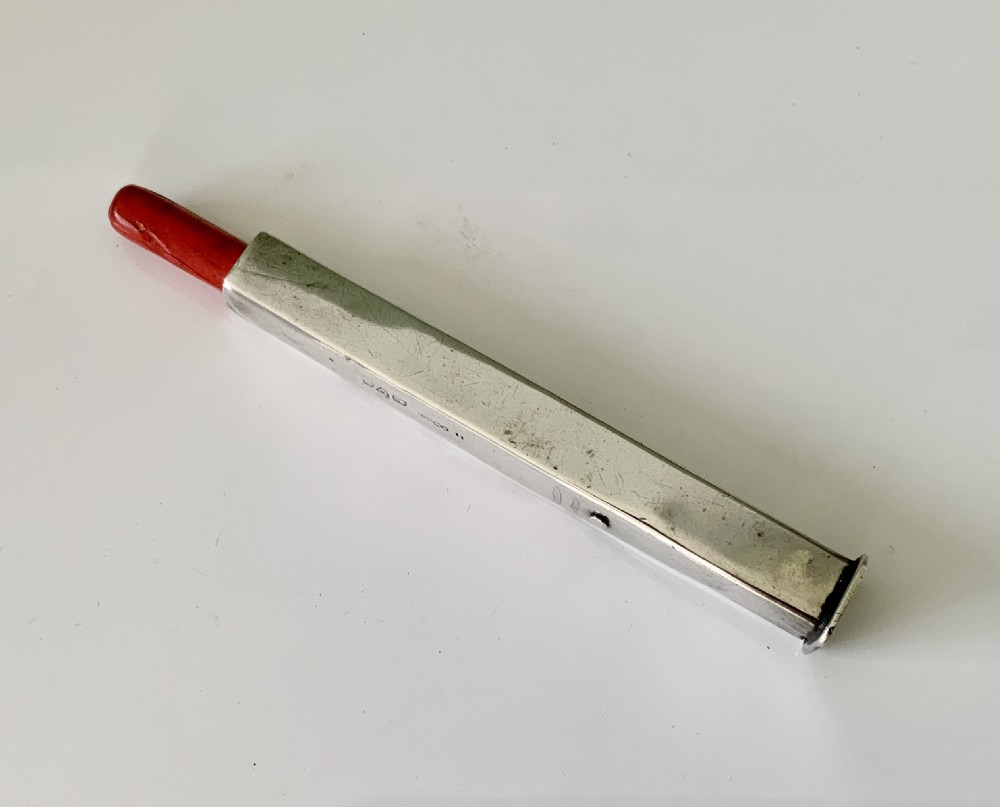 An antique sterling silver rectangular wax holder sheath with visible hallmarks containing a stick of red sealing wax.