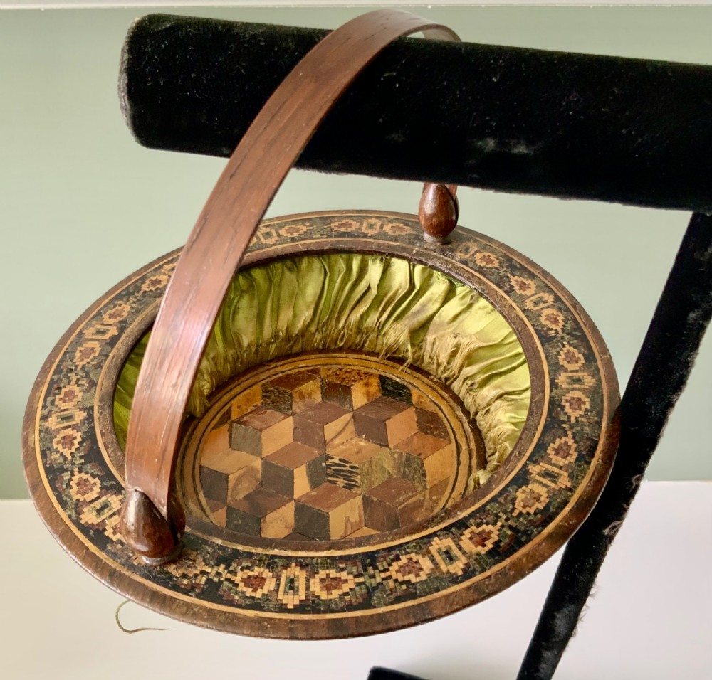 A circular Regency era wooden sewing basket featuring geometric Tunbridge Ware mosaic inlay along the rim, an optical cube parquetry base, green pleated silk interior lining, and an arched handle. View VIII