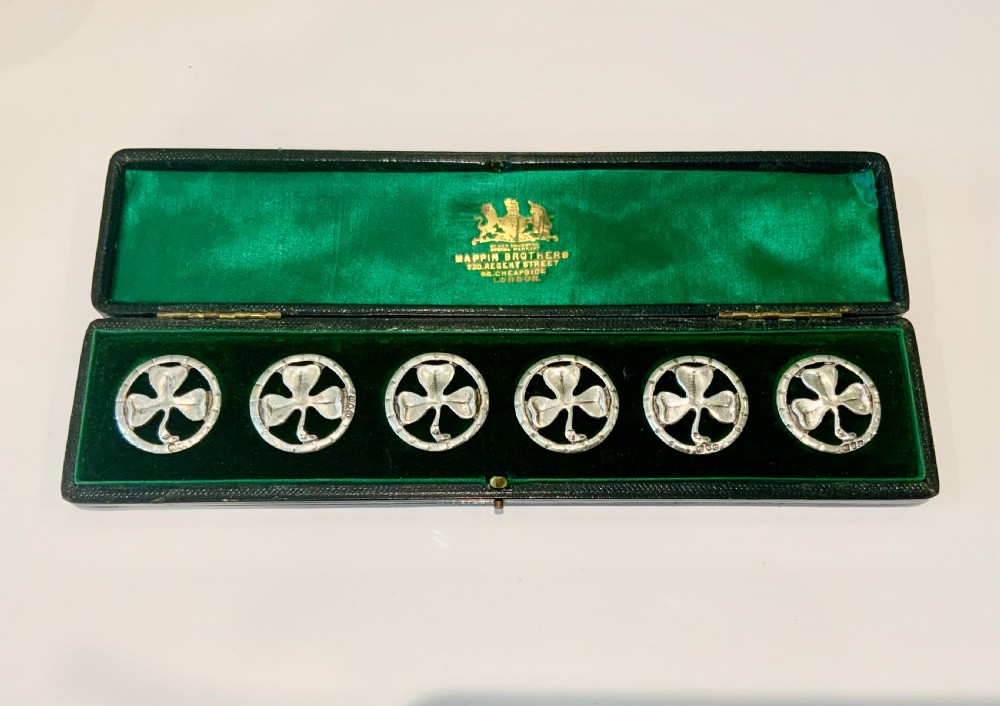 A boxed set of six circular silver buttons featuring a pierced shamrock design inside a dark green velvet-lined presentation case.