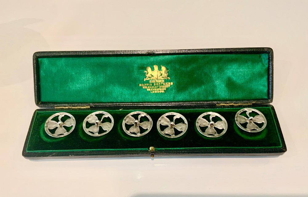 A boxed set of six circular silver buttons featuring a pierced shamrock design inside a dark green velvet-lined presentation case. View II