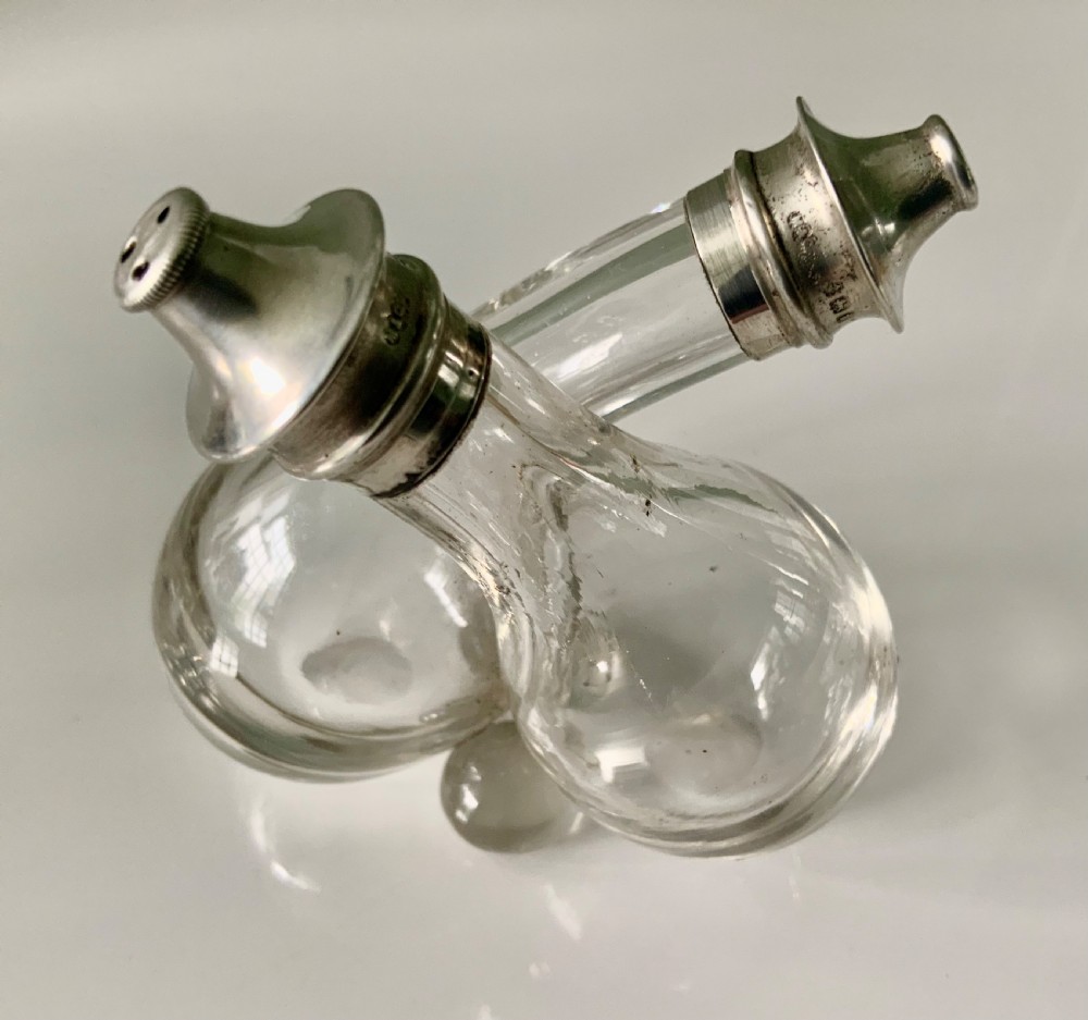 A clear glass double cruet bottle with hallmarked silver tops joined together in an intertwined design. View III