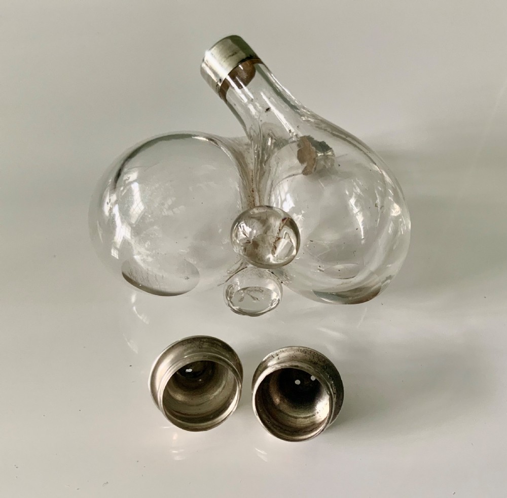 A clear glass double cruet bottle with hallmarked silver tops joined together in an intertwined design. View V