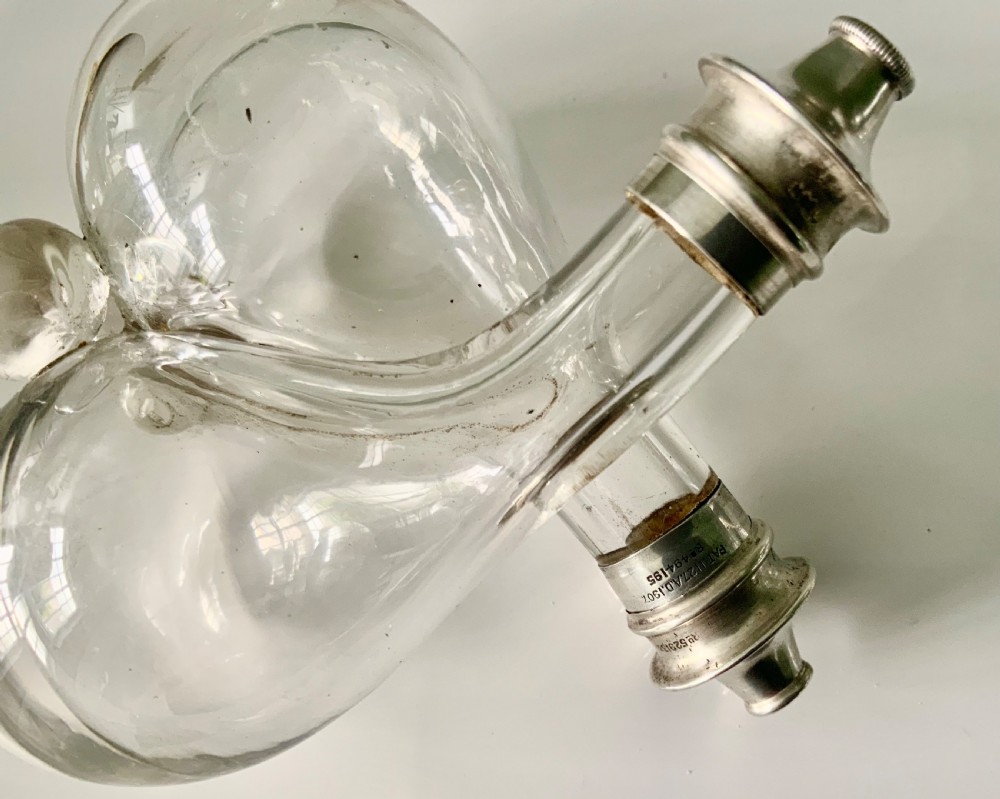 A clear glass double cruet bottle with hallmarked silver tops joined together in an intertwined design. View VI