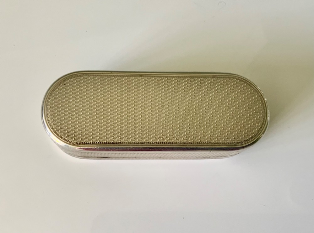 An elongated oval sterling silver snuff box featuring fine engine-turned surface pattern and a central engraved crest shield. View VII