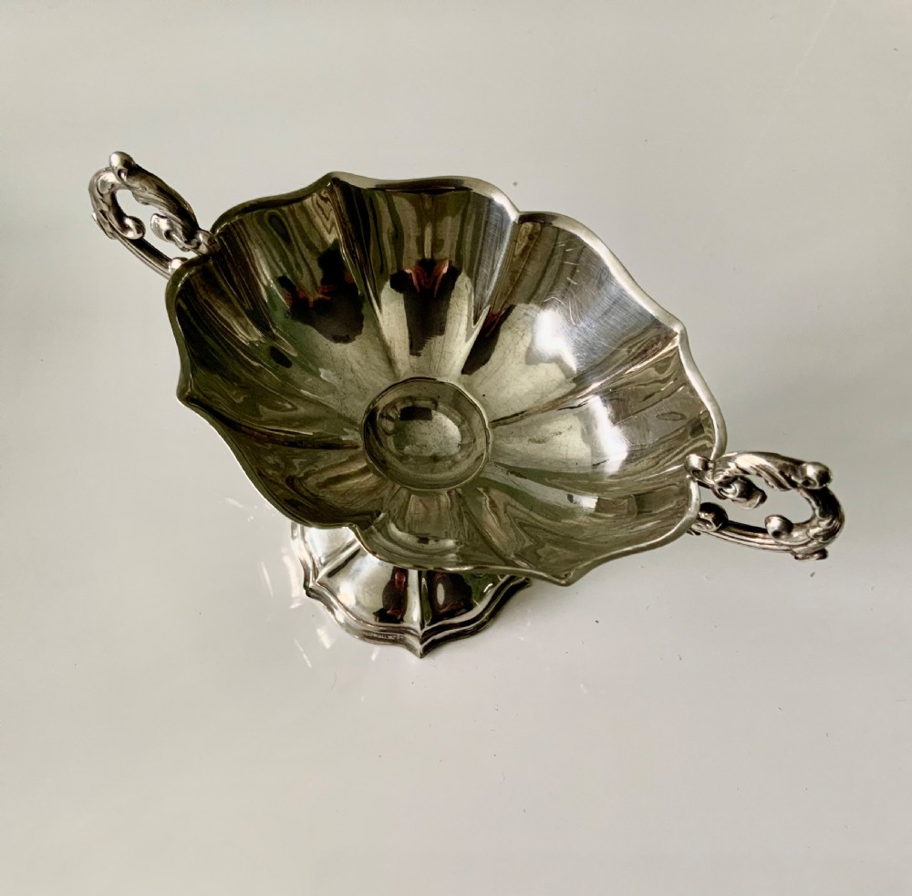 A polished silver dish featuring a lobed rim, two ornate scroll handles, and a central swan motif on a flared pedestal base. View V