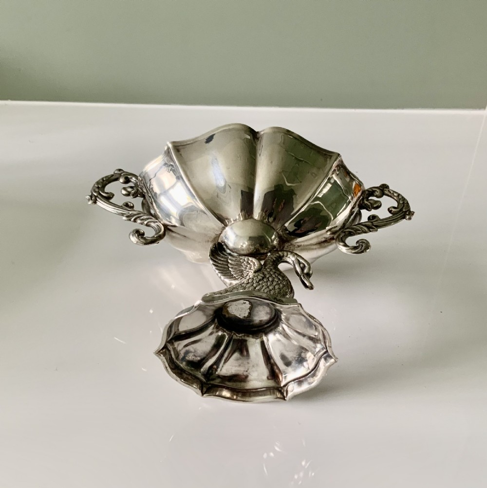 A polished silver dish featuring a lobed rim, two ornate scroll handles, and a central swan motif on a flared pedestal base. View VI
