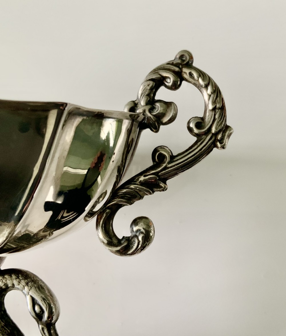 A polished silver dish featuring a lobed rim, two ornate scroll handles, and a central swan motif on a flared pedestal base. View VIII